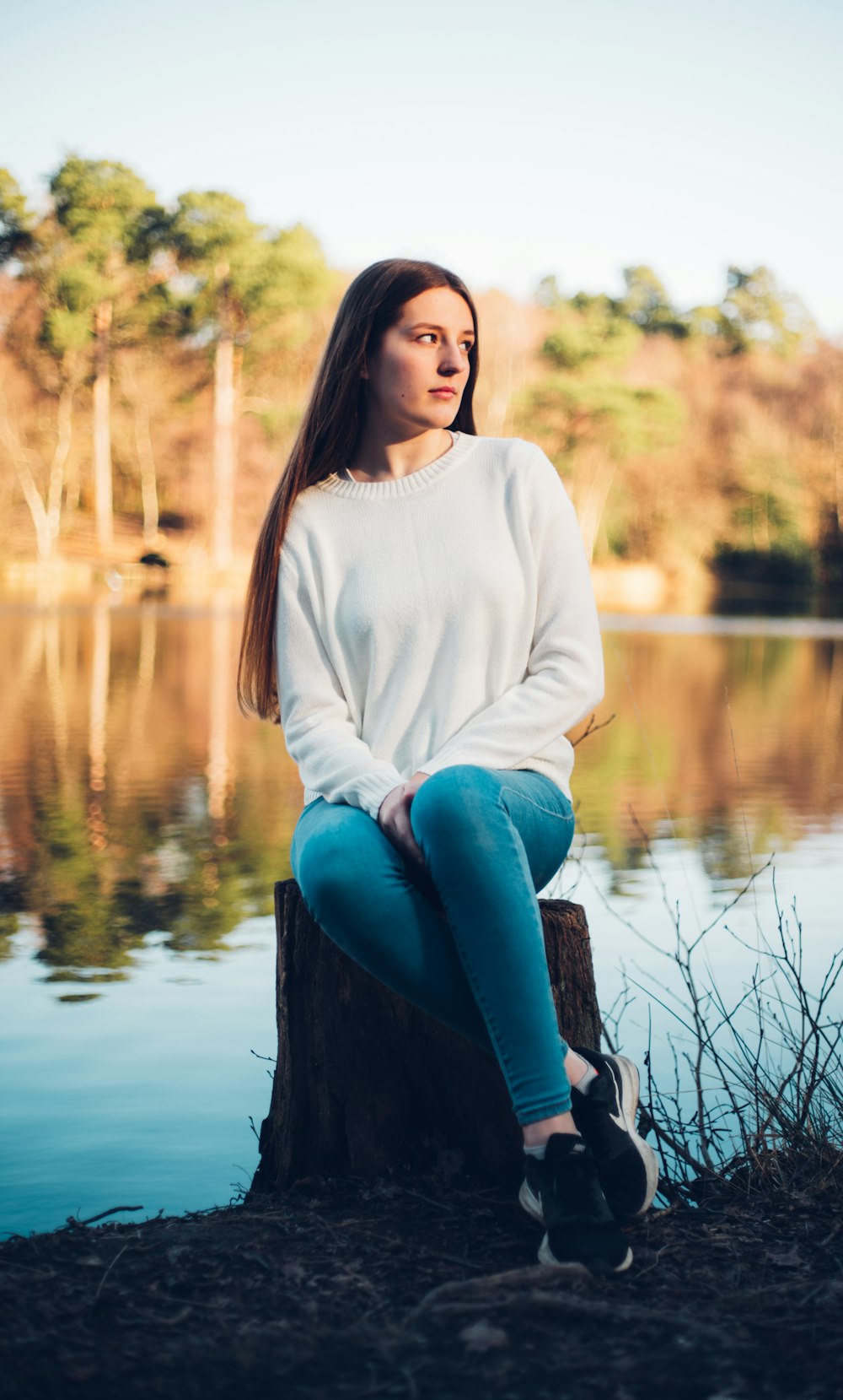 Frau in weißem Langarmhemd und blauer Jeans sitzt auf braunem Holzstamm nahe nahe nahe nahe nahe