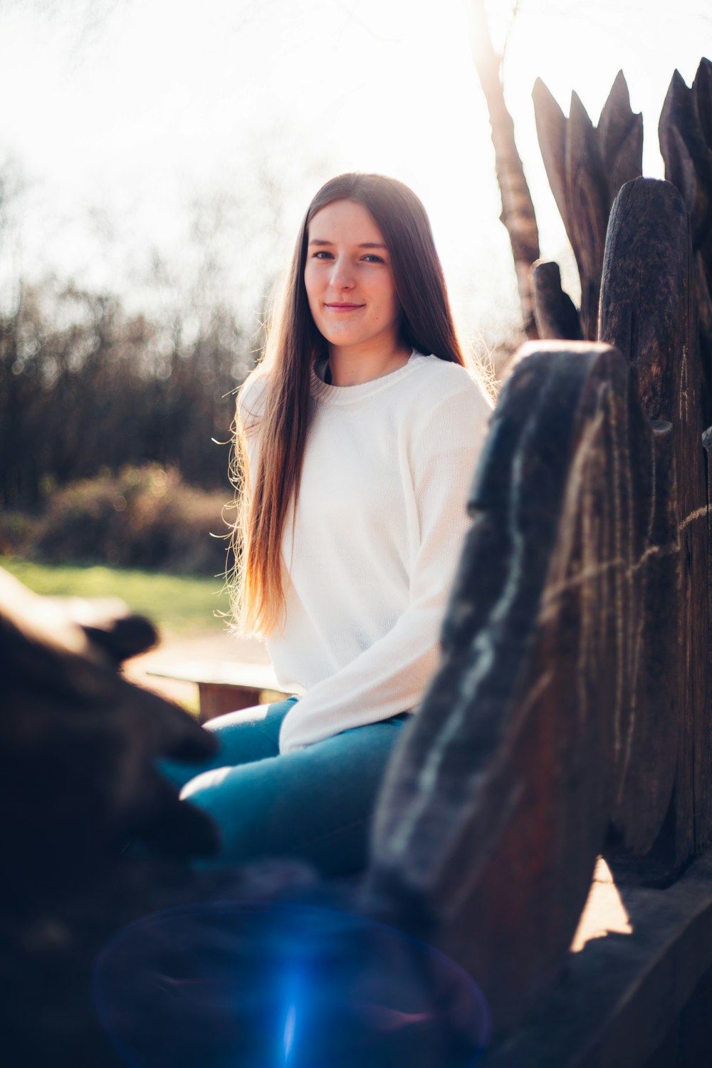 woman in white long sleeve shirt and blue denim jeans sitting on brown wooden bench during