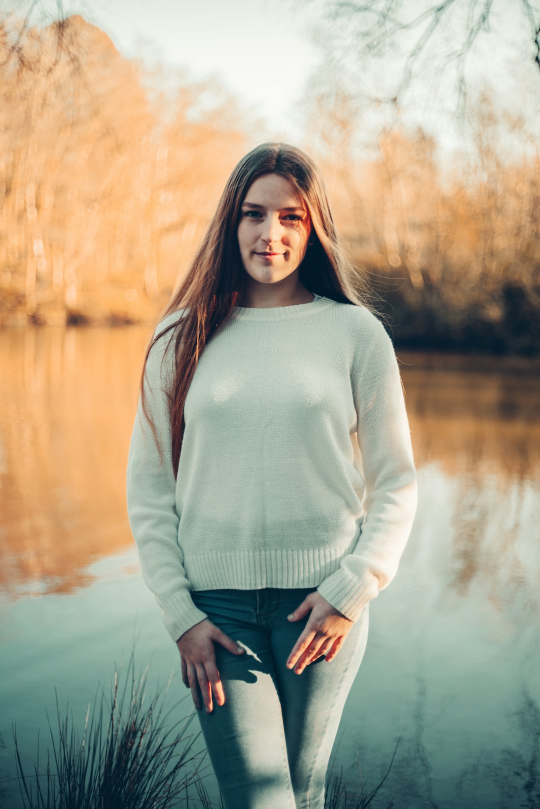 woman in gray long sleeve shirt and blue denim jeans standing near lake during daytime