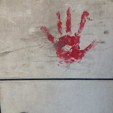 A handprint in red paint is smeared on a concrete wall. The wall has visible lines and a slightly rough texture with some marks and scratches.