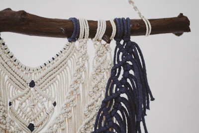 Close-up of a delicate cream-colored macrame wall hanging with intricate knots and wooden beads.