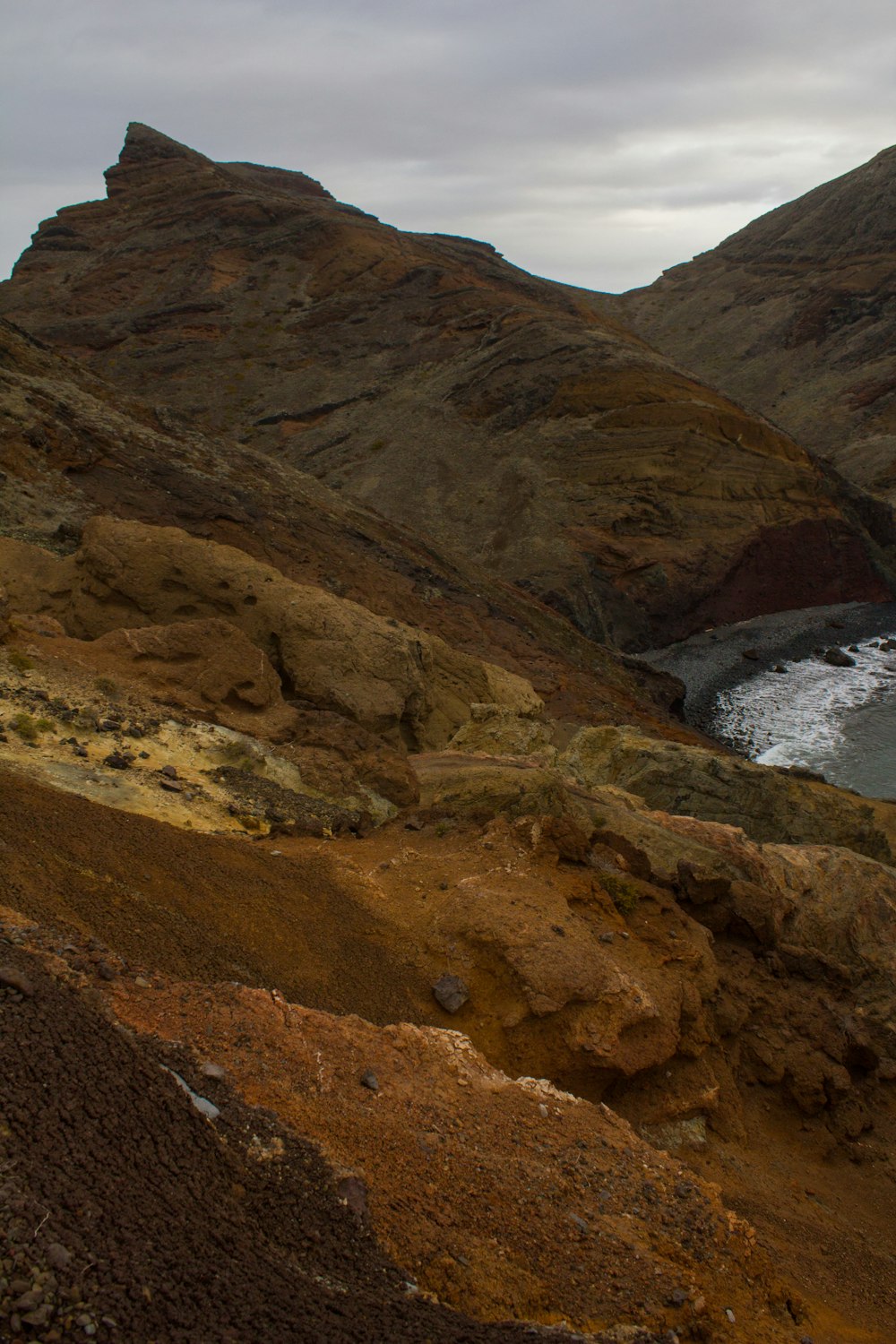 brown mountain beside body of water during daytime