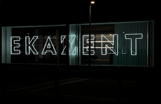 Close-up of a sleek, illuminated 3D letter sign glowing against a dark industrial background.