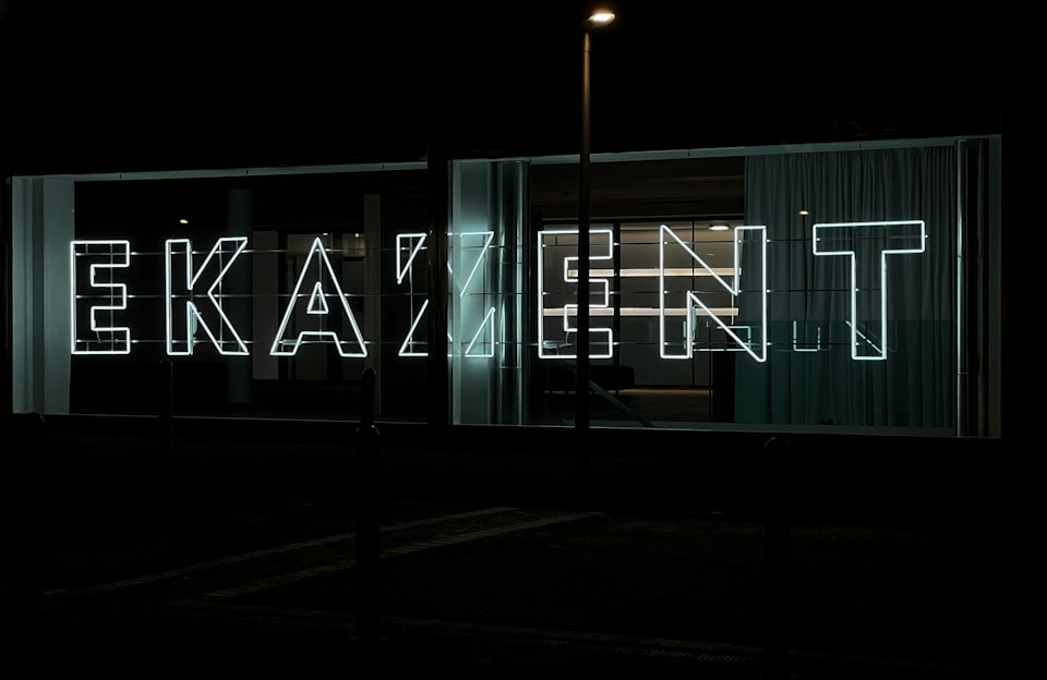 A sleek acrylic sign glowing with soft white light in a modern commercial plaza setting