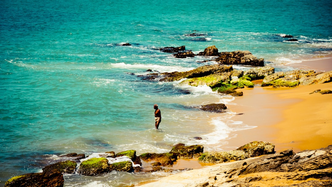 woman in black bikini standing on brown rock formation near body of water during daytime