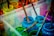 A collection of paint jars in various vibrant colors, including blue, green, and pink. Wooden paintbrushes covered in paint rest inside the jars, and the splattered paint around them suggests creative activity. The scene is set in a transparent plastic container.