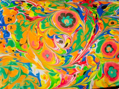 Vibrant and swirling patterns of colors including orange, green, yellow, blue, and red, mixed with floral shapes that create a psychedelic and dynamic visual effect.