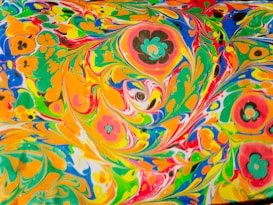 Vibrant and swirling patterns of colors including orange, green, yellow, blue, and red, mixed with floral shapes that create a psychedelic and dynamic visual effect.