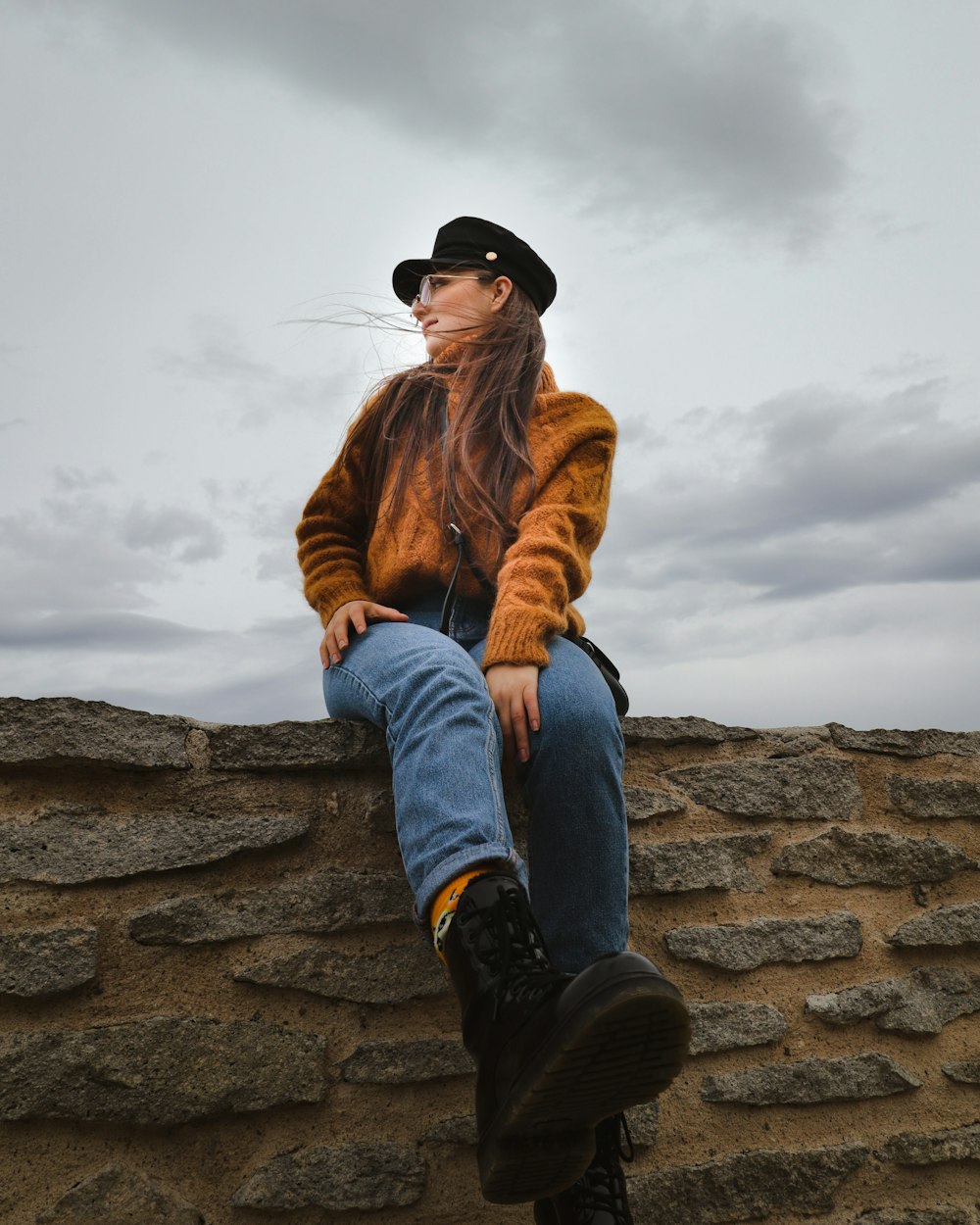 woman in brown jacket and blue denim jeans sitting on rock