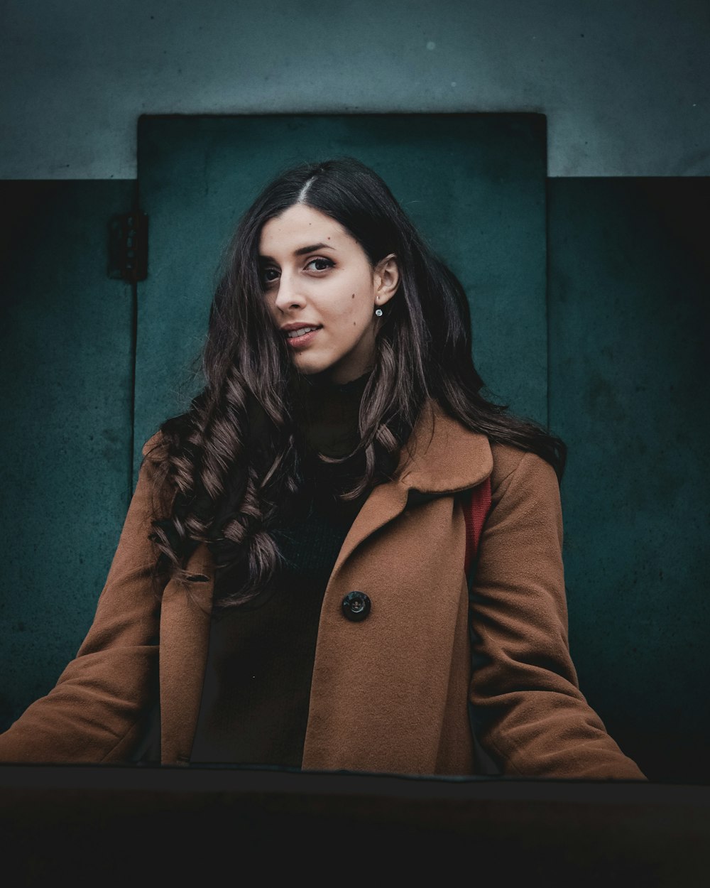 woman in brown coat standing near green wall