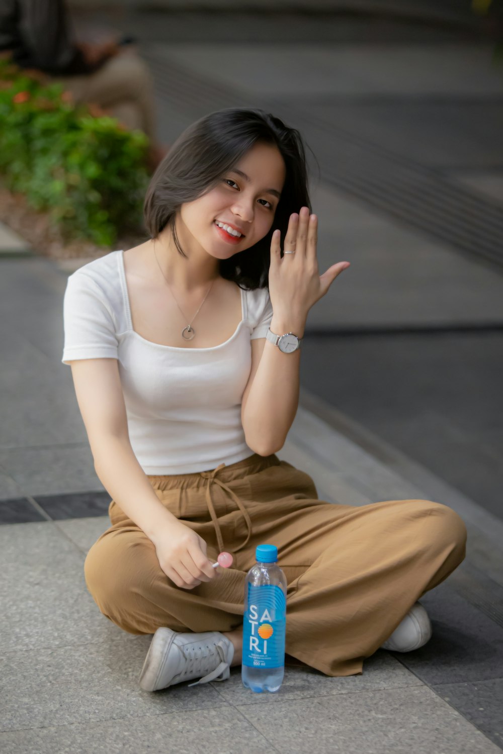woman in white scoop neck shirt and brown pants sitting on gray concrete floor