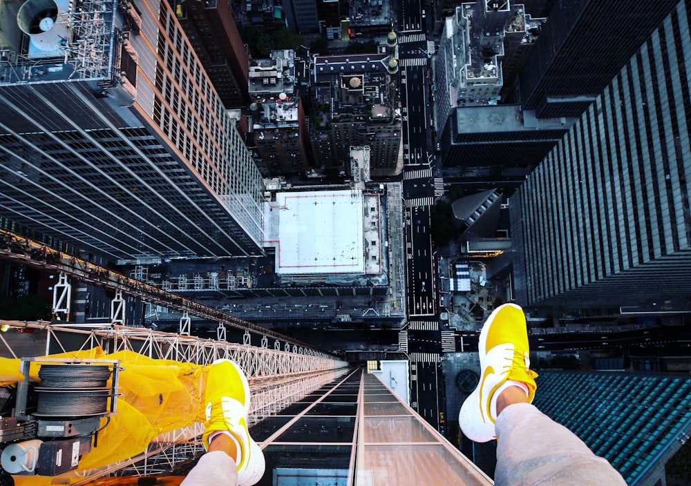 person in white pants and yellow sneakers sitting on the edge of a building