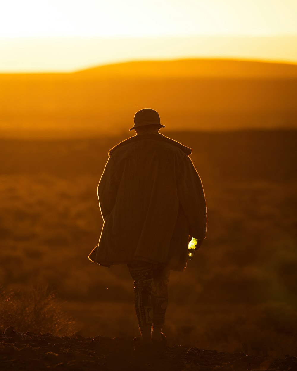 Hombre con chaqueta negra de pie en un campo marrón durante la puesta de sol