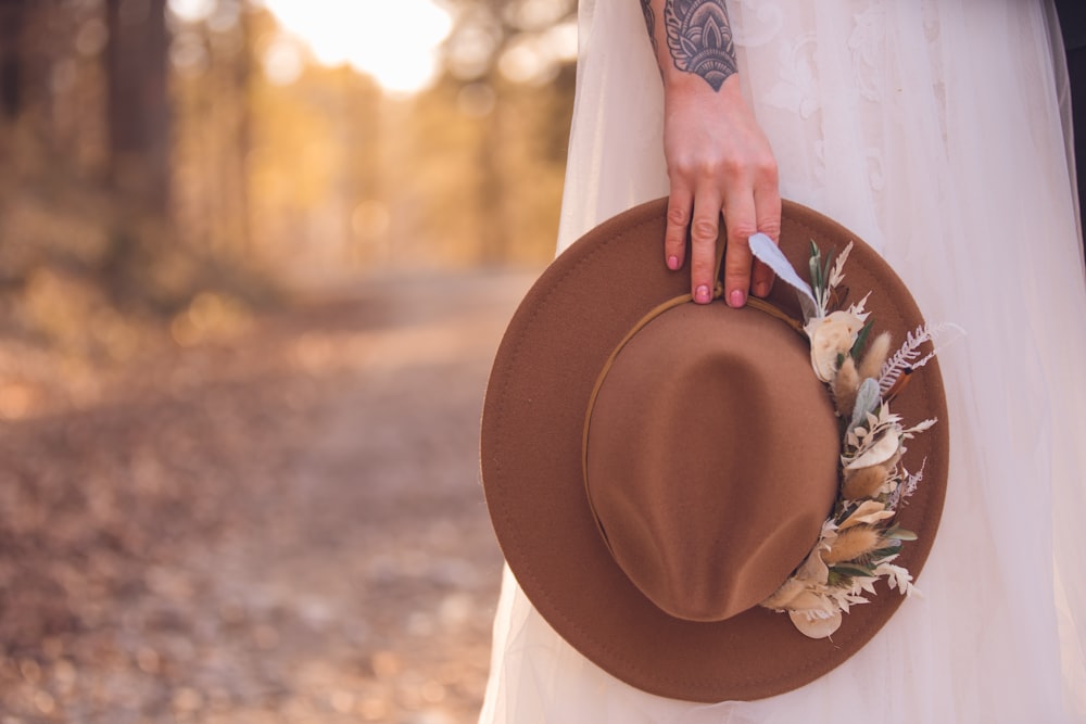 Femme en chemise blanche à manches longues tenant un chapeau marron