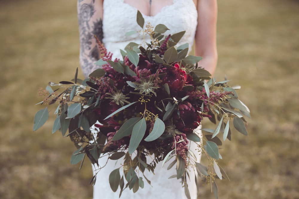 donna in abito da sposa in pizzo floreale bianco che tiene la pianta rossa e verde