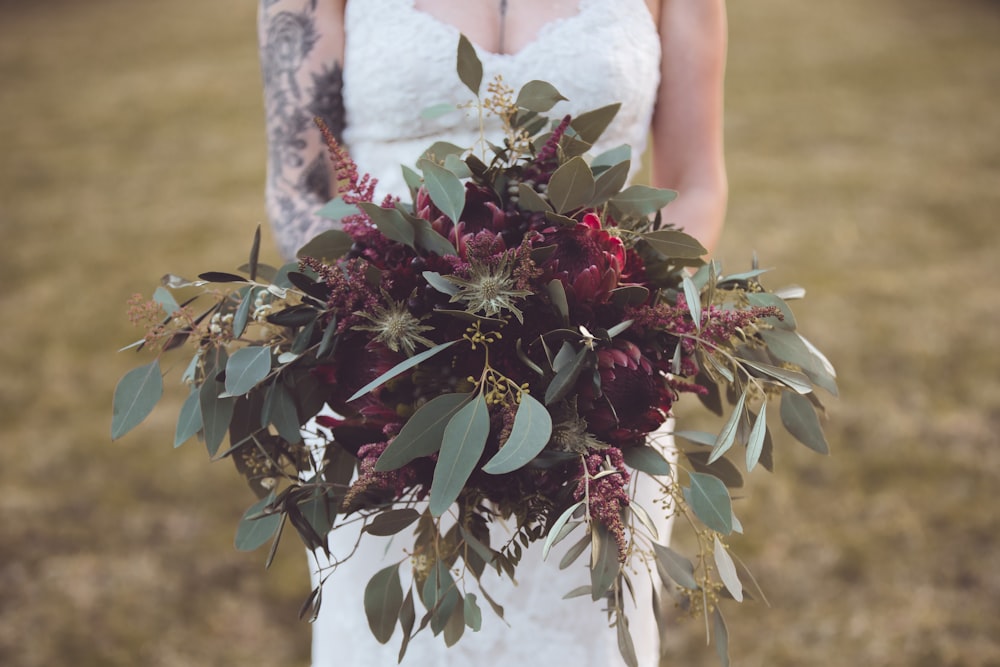 Mujer en vestido de novia de encaje floral blanco sosteniendo planta roja y verde