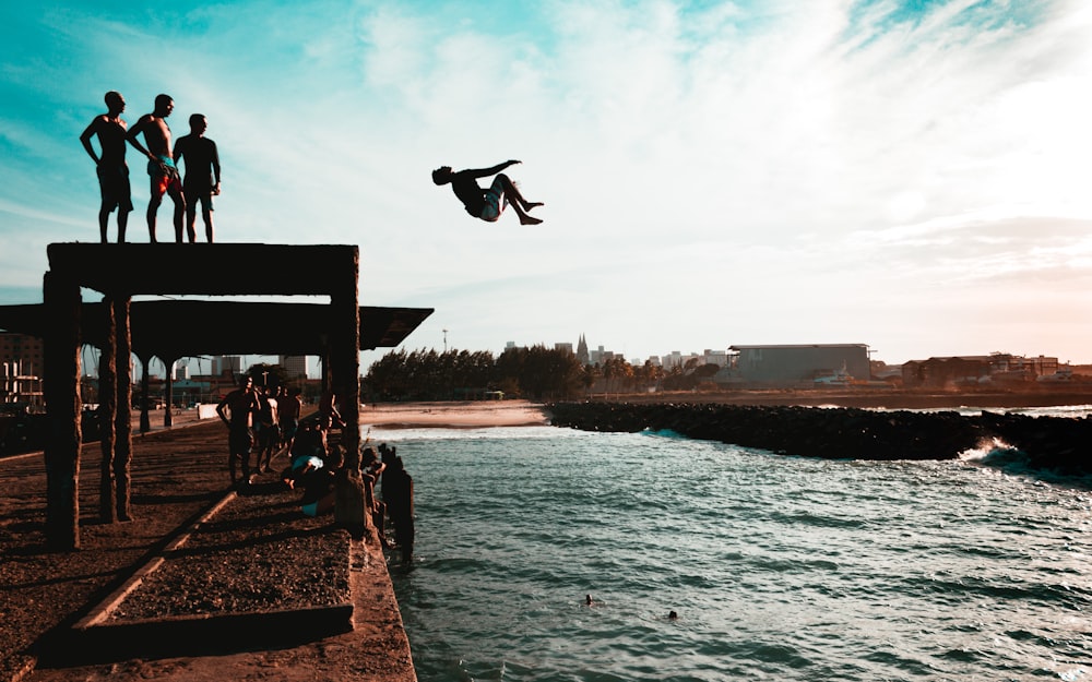 man jumping from a cliff to a lake