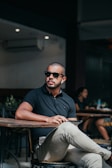 Man sitting at a café table, sporting a red stripe polo and sipping coffee.