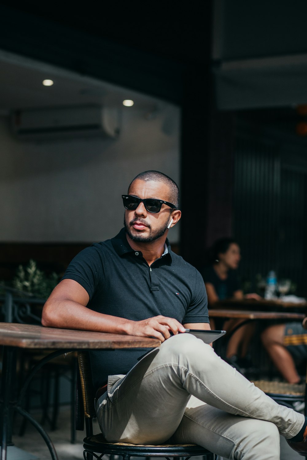 Homme en polo noir portant des lunettes de soleil noires assis sur une chaise