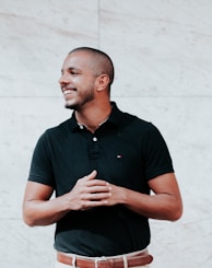 man in black polo shirt standing near white wall