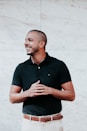 man in black polo shirt standing near white wall