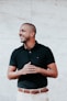 man in black polo shirt standing near white wall
