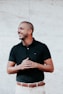 man in black polo shirt standing near white wall