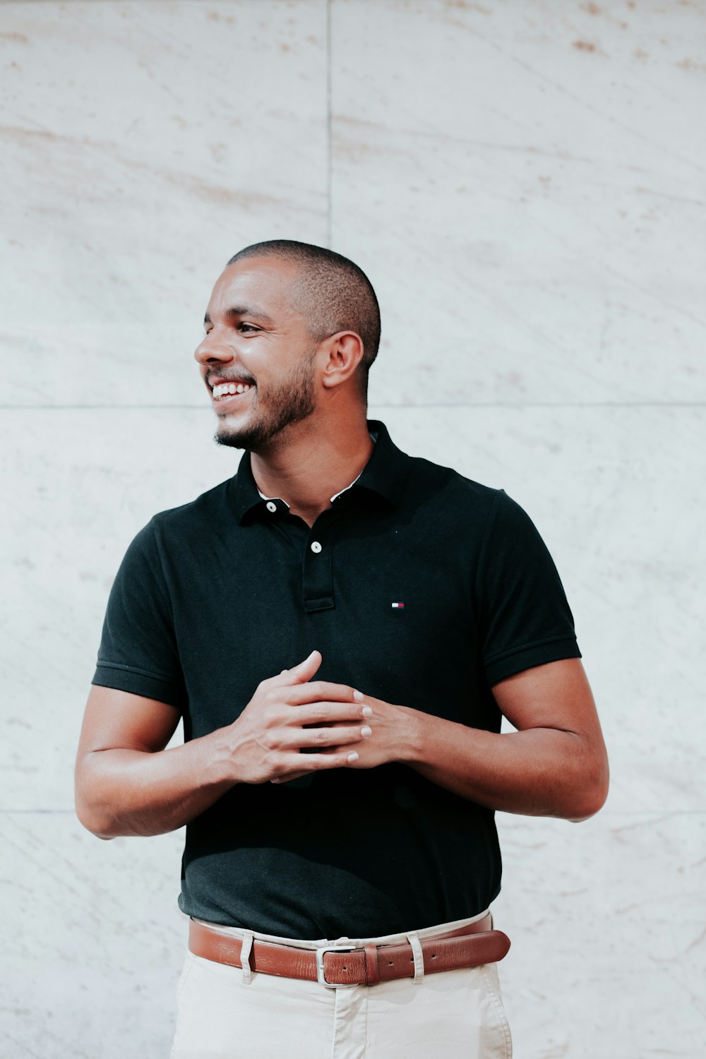 man in black polo shirt standing near white wall