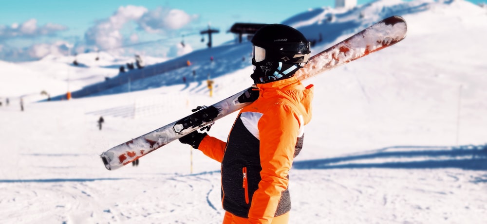 man in orange jacket and pants standing on snow covered ground during daytime