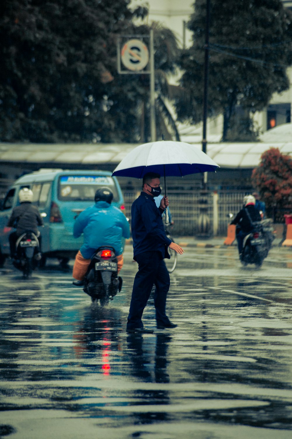 man in black jacket and black pants holding umbrella walking on wet road during daytime