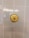 A close-up view of a white tiled wall with a brass circular fixture mounted at the center. The fixture has a smooth, glossy appearance, with concentric circular patterns. The tiles are neatly lined up in a grid pattern and exhibit a slight reflection.