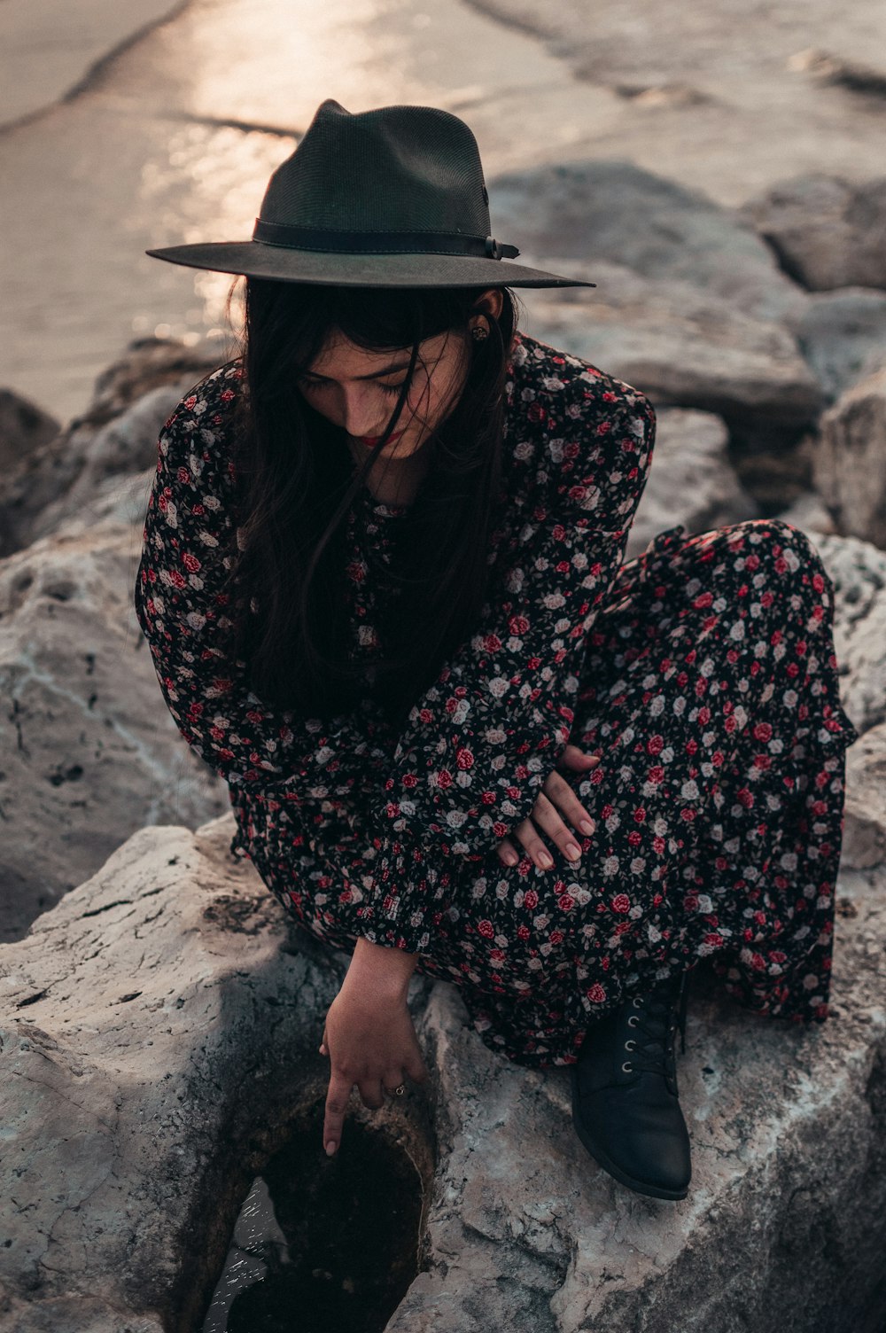 woman in black and white long sleeve shirt wearing black hat sitting on gray rock during