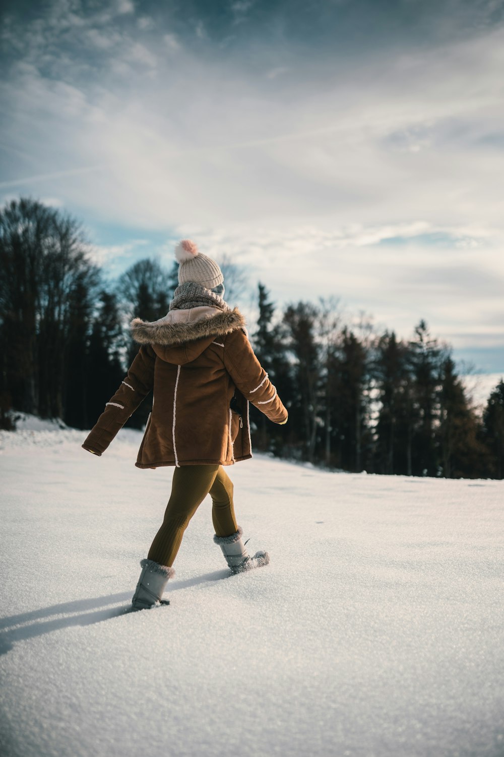 woman in brown coat and brown pants standing on snow covered ground during daytime