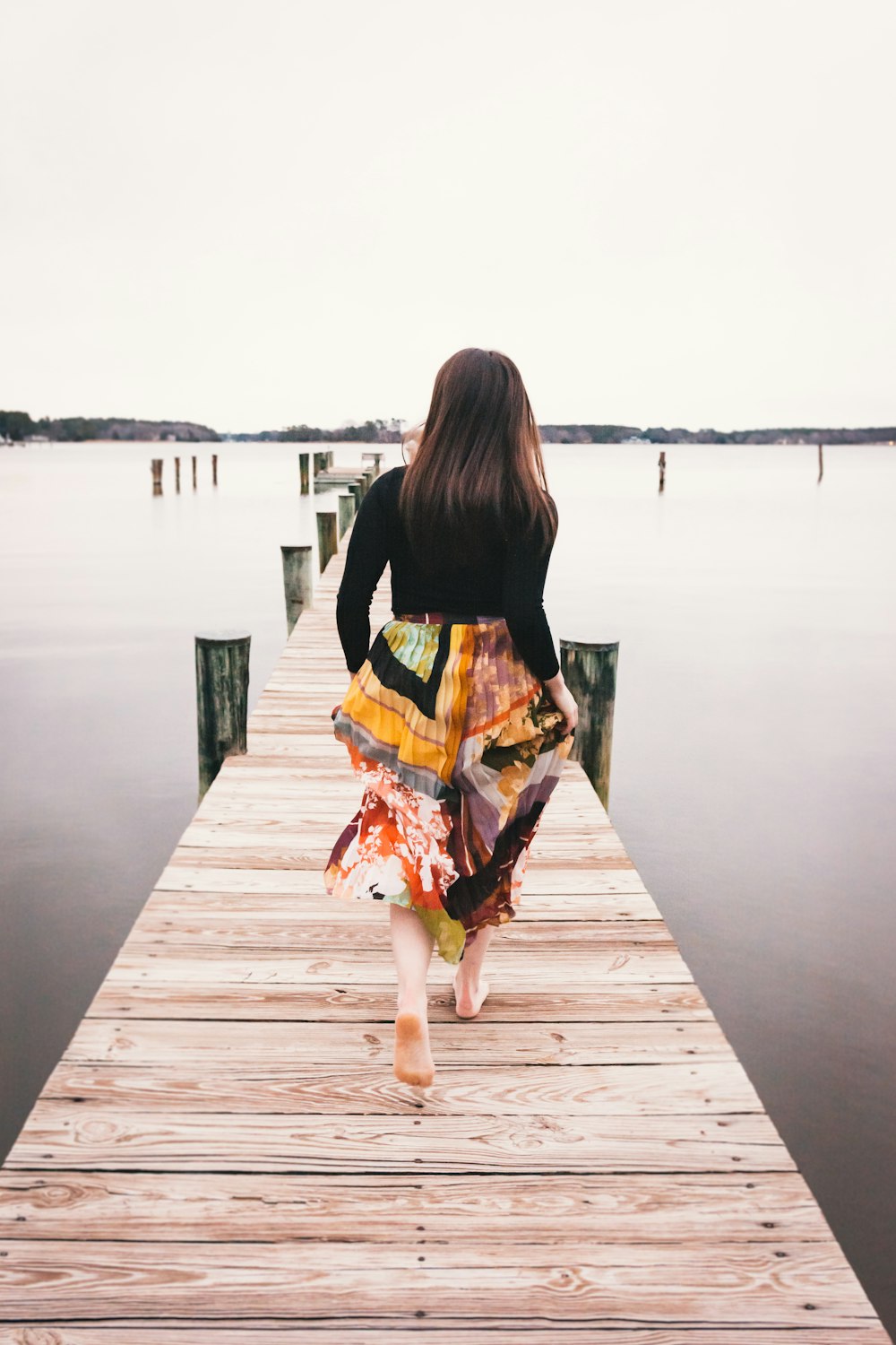 woman in black long sleeve shirt and orange skirt walking on wooden dock during daytime