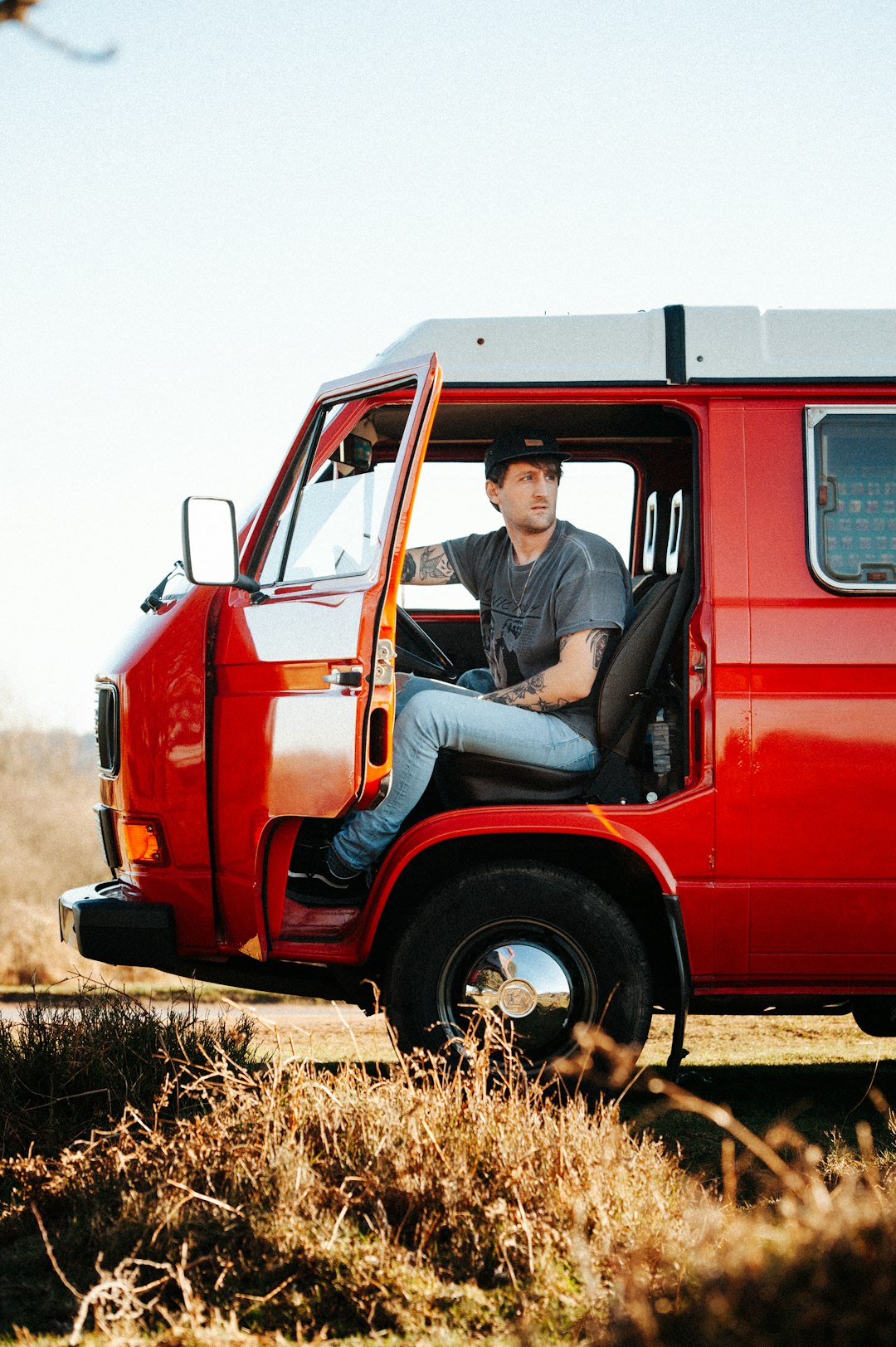 man in blue denim jacket sitting on red and white van