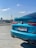 A bright blue BMW M235i is parked on what appears to be a rooftop or parking lot, with a clear blue sky and a television tower in the background. The car's license plate is visible, and the area appears calm and sunny.