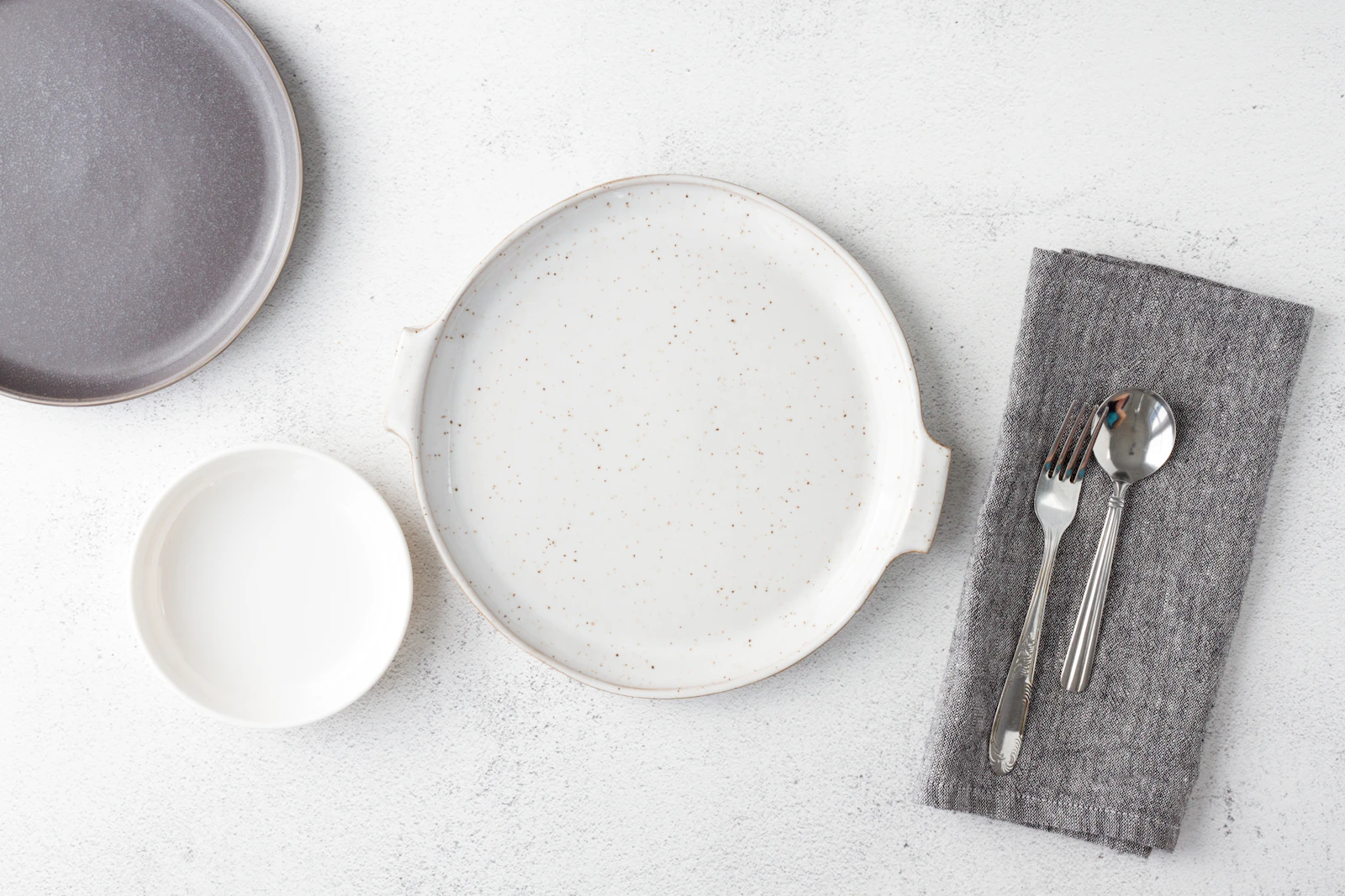 A stack of hand-thrown oat-glazed stoneware dinner plates on a pale linen cloth