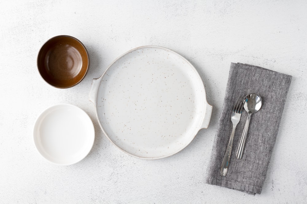 Assiette en céramique blanche à côté d’une fourchette en acier inoxydable et d’un couteau à pain