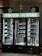 A wine refrigerator with three sections, each filled with various bottles of wine and spirits. The top portion displays the phrase 'Truth in Dirt' in illuminated letters. Several bottles are lying horizontally on the shelves, showcasing their labels. Glass bottles, likely empty, are also visible at the base. The fridge is set against a dark background with additional wine bottles stored on shelves to the left.