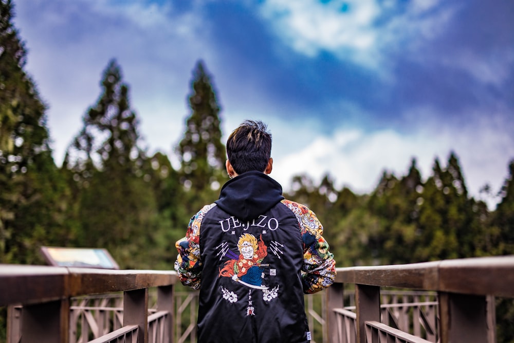 person in black and yellow floral hoodie standing on wooden bridge during daytime