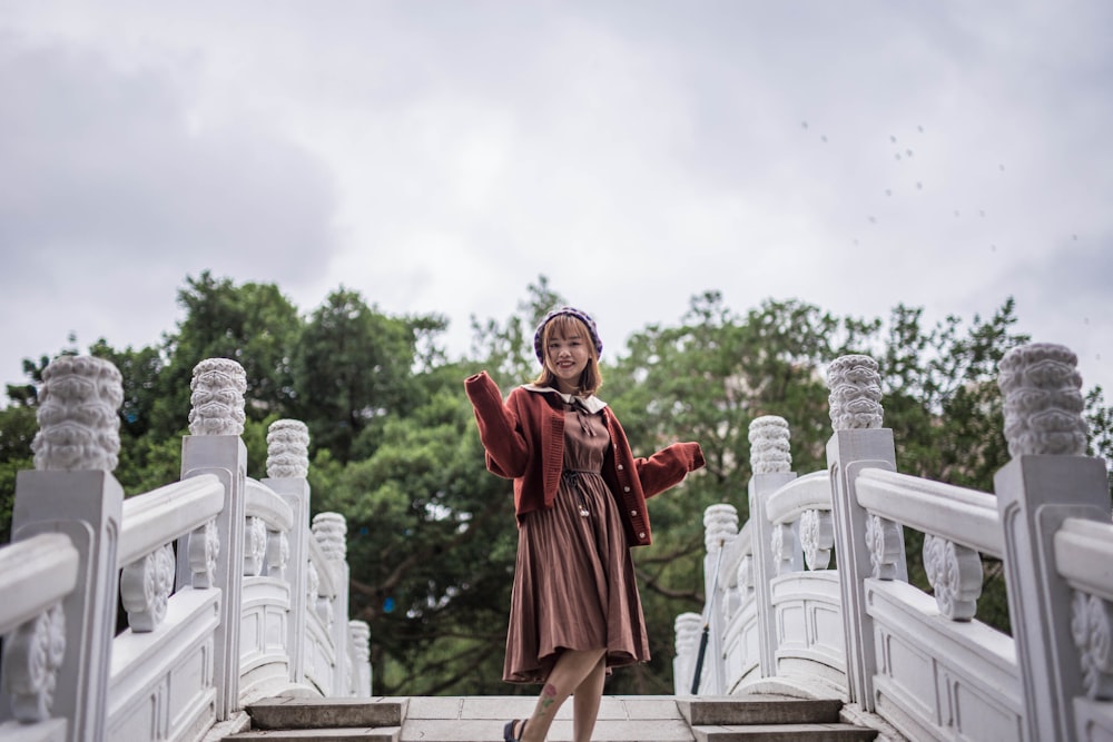 woman in red long sleeve dress standing on gray concrete fence during daytime