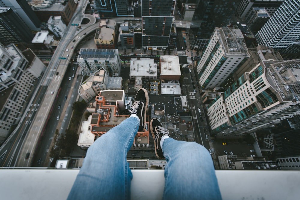 person in blue denim jeans and black sneakers sitting on white concrete building during daytime