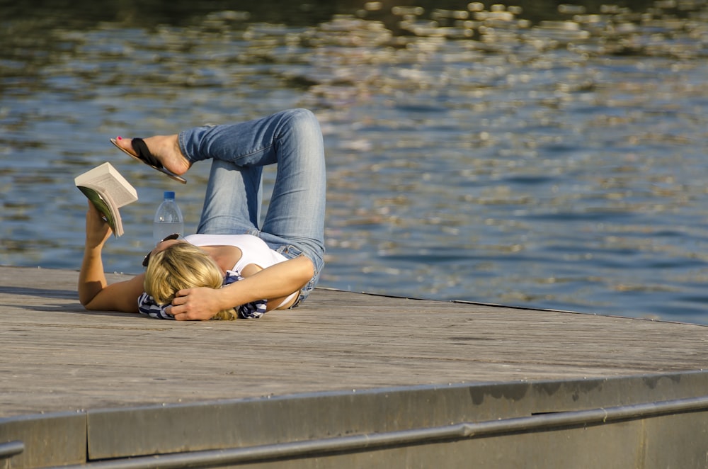 femme en débardeur blanc et pantalon gris couché sur un quai en bois brun pendant la journée