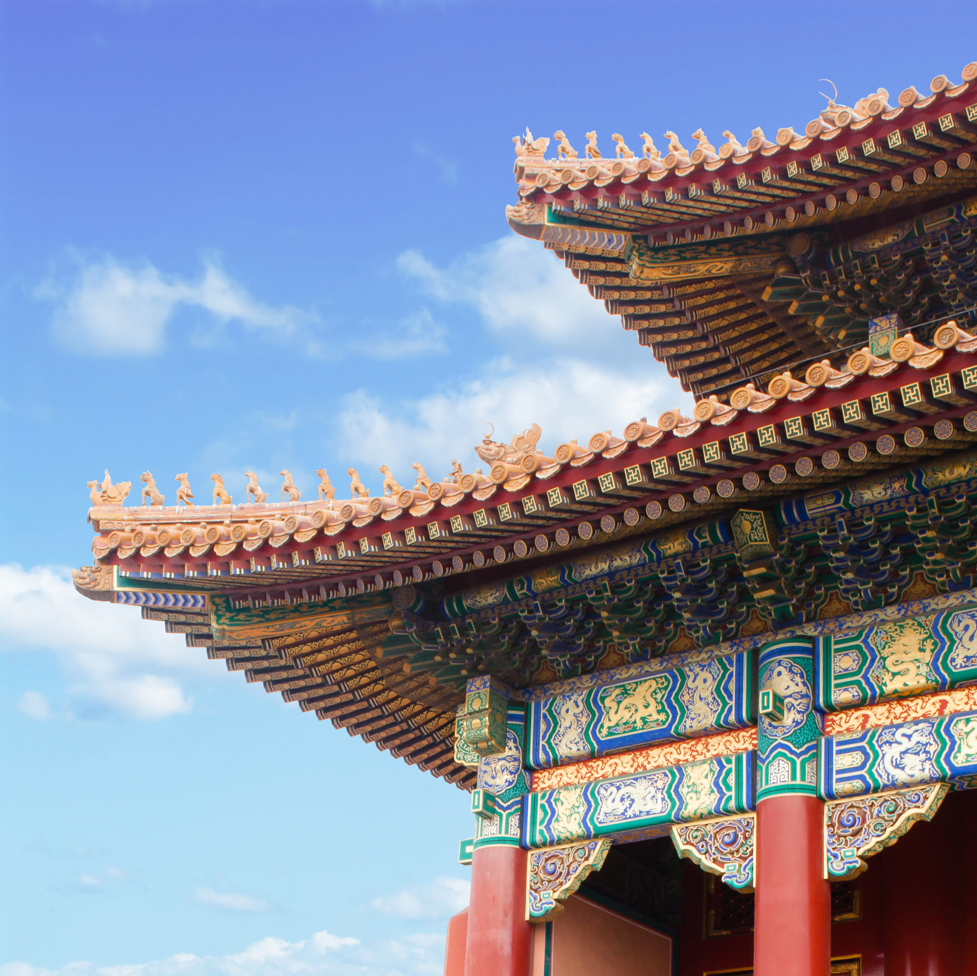 Close-up of an ornate red, green and gold upturned roof eave against a clear blue sky on a Beijing palace building.