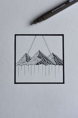 A black ink drawing depicting a stylized mountain landscape within a square frame. The mountains are rendered with intricate linework, and two diagonal lines extend upward from the peaks. A black ink pen is positioned diagonally above the drawing, suggesting a creative process in progress.