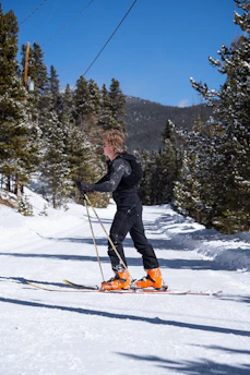A skier adjusting their colorful ski boots beside a mountain lodge at sunrise