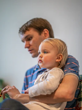 A father working on a laptop while caring for his child nearby.