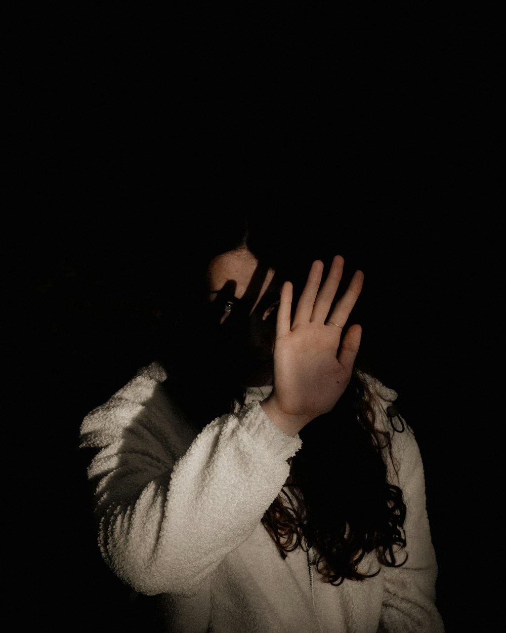 woman in white long sleeve shirt covering her face with her hands