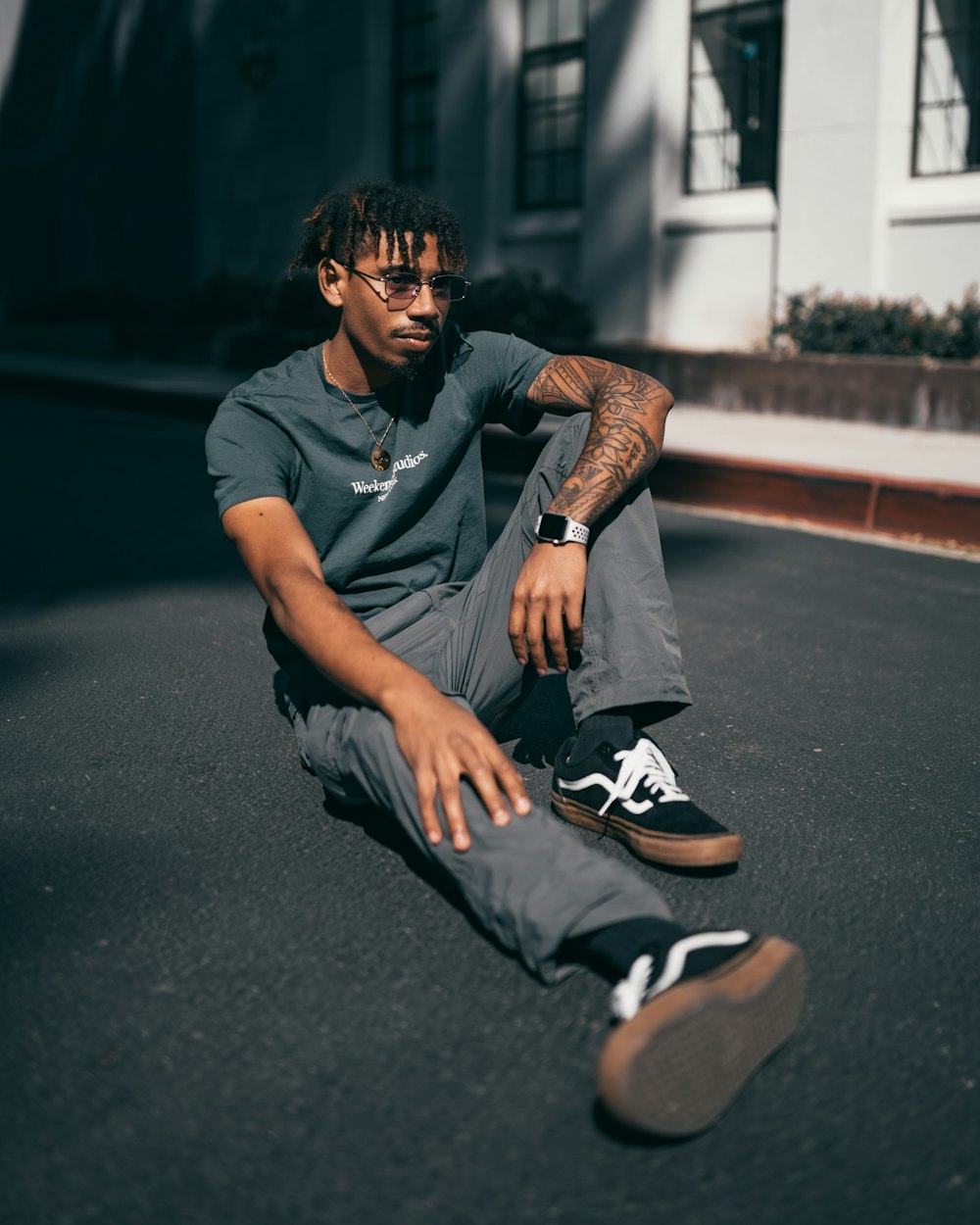 man in black crew neck t-shirt and gray shorts sitting on gray asphalt road during