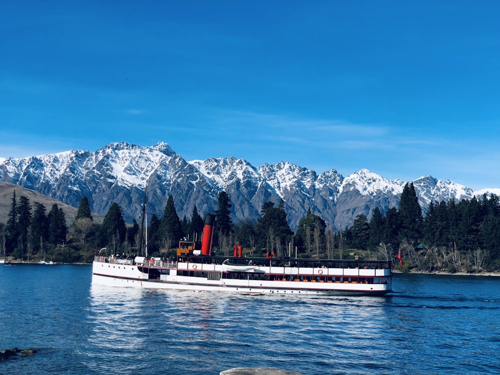 weißes und rotes Boot tagsüber auf dem Wasser in der Nähe des Berges